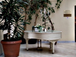 [picture: White grand piano with candelabra and large potted plant]